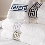 Stack of luxury white towels with elegant embroidered border designs in a cozy hotel room setting