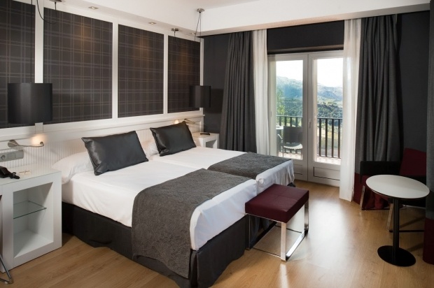 Modern hotel room with a view of the mountains, featuring a double bed, elegant dark curtains, and contemporary furnishings.
