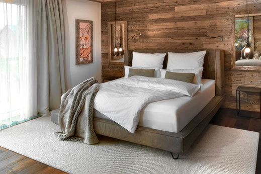 Cozy rustic bedroom interior with wooden wall cladding, plush queen-size bed with white linen and pillows, and a soft gray throw blanket